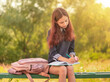 Girl teenager schoolgirl writes in a notebook sitting on a bench.