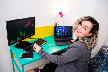 young woman smiles satisfied while analyzing financial charts on monitor, laptop and cell phone