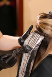 Professional female hairdresser applying color to female customer at design hair salon, woman having her hair dyed, Hair dye colouring in process