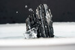 Closeup of a black tourmaline minerals with water droplets on a white surface
