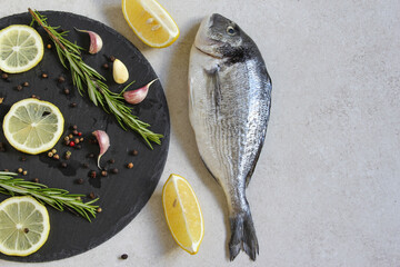 One fresh raw sea organic dorado or sea bream with spices and lemon on a grey background