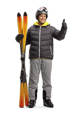 Canvas Print - Full length portrait of a young man holding a pair of skis and gesturing a thumb up sign