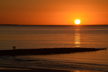 Vibrant golden sunset shining upon the beach with two people talking along the shore