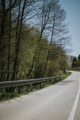 Poster - Vertical shot of an empty highway road along safety steel barrier against blue sky