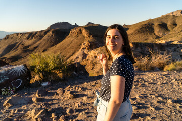 Poster - Young smiling Caucasian female standing in the background of hills under a blue clear sky at sunset