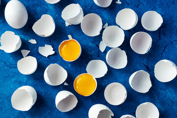 there are many white eggshells on a blue background. in two shells there is a yolk from an egg