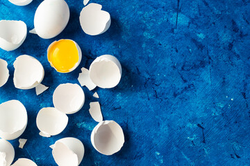 Wall Mural - there are many white eggshells on a blue background. there is an egg yolk in one shell