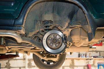 Rear wheel hub of a car lifted on a lift. In the garage, a man changes parts on a vehicle. Small business concept, car repair and maintenance service. UHD 4K.