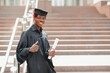 young african male graduate standing in front of university building