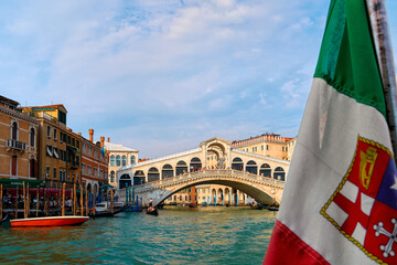 Beautiful view of Italian maritime flag and bridge of Rialto or ponte Rialto on Grand Canal on Venice, Italy. Gondola service station on the left.