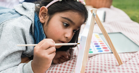 Wall Mural - happy indian little girl having fun painting outdoor at city park - main focus on girl face