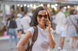© sutlafk - Happy young travel asian woman using mobile phone and relax on street chatuchak weekend market in bangkok, holiday with bags, sunglasses,Thailand, Travel vacation city concept.