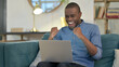 © stockbakers - Successful Young African Man with Laptop Celebrating on Sofa