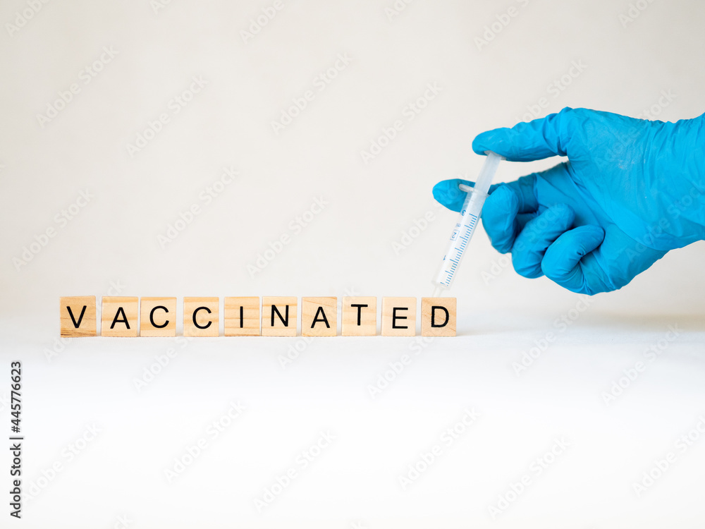 vaccinated - słowo ułożone z drewnianych kostek, strzykawka i ręka - obrazy, fototapety, plakaty 