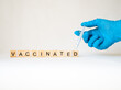 vaccinated - słowo ułożone z drewnianych kostek, strzykawka i ręka