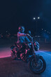 Motorcyclist sits on a motorbike in neon light in an empty parking lot at night