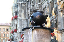 A Real Dove Against The Background Of A Large Bronze Fish. Fish Fountain At Marienplatz (Marian Square). Main Square Of The Munich, Germany.