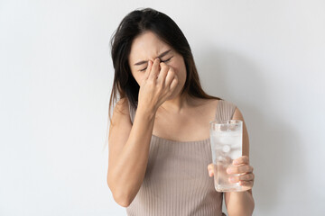 Portrait of young Asian woman has brain freeze after drink iced water. Girl feel terrible headache with a glass of cold water on white background. Copy space