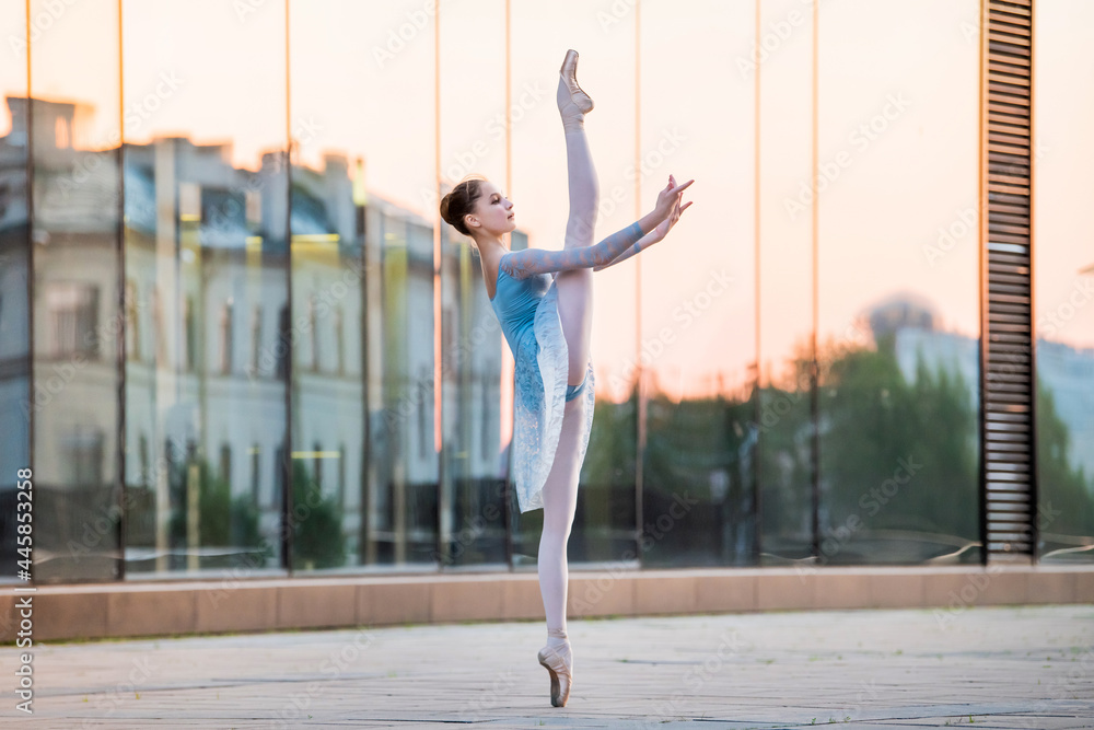 young ballerina dancing on pointe shoes against backdrop of the reflection of sunset in the city - obrazy, fototapety, plakaty 