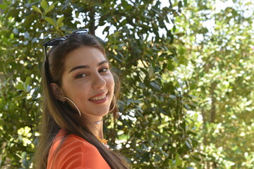 Wall Mural - Young girl smiling in the garden. Young women portrait. Garden background with trees. Summer season