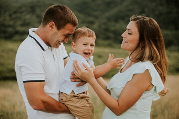 Wall Mural - Young family with cute little boy having fun outdoors in the field