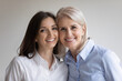 © fizkes - Head shot cheek to cheek portrait of happy senior 60s mother and young grownup daughter. Cute teen millennial granddaughter and beloved grandmother smiling at camera. Intergenerational relations
