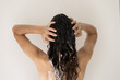 © fizkes - Back view of millennial female brunette with long thick wavy hair take shower wash head use revitalizing shampoo balsam with keratin. Rear shot of young woman doing routine hygienic bath procedures