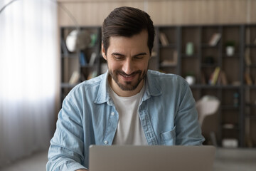 Wall Mural - happy young caucasian man working on computer at modern home office. smiling millennial guy reading 