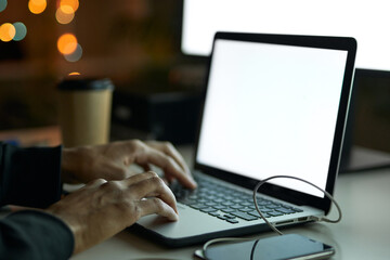 Close up shot of hands of man sitting at the table in front of computer monitor and using laptop while working late at night