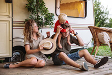 Family Trip, Caravan Camping Lifestyle And Recreation: Young Parents Relaxing With Small Son At Camper House Having Vacation In Forest, Picnic Outdoors Or Road Journey In Mobile Home Or Retro Trailer