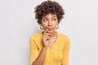 © WHstudio Leushin N - Horizontal shot of thoughtful young African American woman looks aside has dreamy expression interesting idea in mind wears casual yellow jumper isolated over white background makes decision
