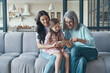 © gstockstudio - Little girl with mother and grandmother using smart phone while sitting on the sofa at home