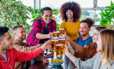 diverse group of friends celebrating happy hour making a toast with pint glasses of beers inside a bar restaurant. multiethnic people together in a pub having a drink. fun, joy and lifestyle concept