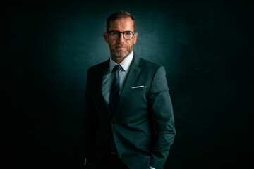 Middle aged businessman wearing suit and tie while standing a isolated dark grey background