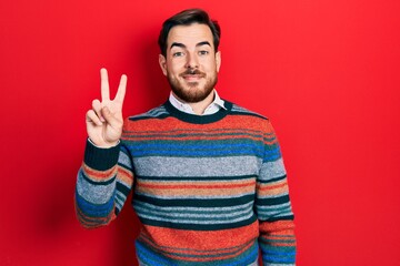 Handsome caucasian man with beard wearing elegant wool winter sweater showing and pointing up with fingers number two while smiling confident and happy.