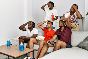 Poster - Young african group of friends sitting on the sofa at home playing video games stressed and frustrated with hand on head, surprised and angry face