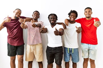 Canvas Print - Young african group of friends standing together over isolated background approving doing positive gesture with hand, thumbs up smiling and happy for success. winner gesture.