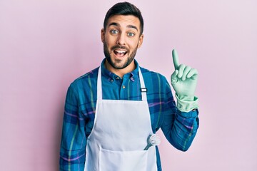 Canvas Print - Young hispanic man wearing apron pointing finger up with successful idea. exited and happy. number one.