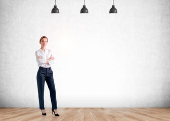 Confident attractive business woman in crossed arm pose and on high heels is pondering how to optimize business process. Full length portrait. Concrete wall, wooden floor, three ceiling lamps.