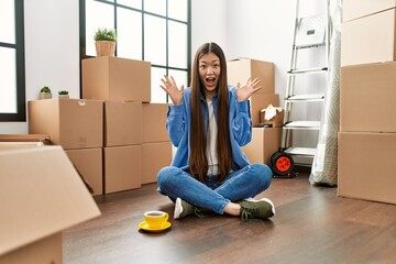 Wall Mural - Young chinese girl sitting on the floor at new home celebrating crazy and amazed for success with arms raised and open eyes screaming excited. winner concept