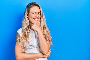 Sticker - Beautiful young blonde woman wearing casual white shirt looking confident at the camera smiling with crossed arms and hand raised on chin. thinking positive.