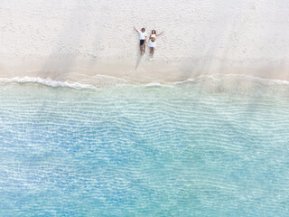 Wall Mural - Young couple traveler sitting and relaxing at beautiful tropical white sand beach with wave foam and transparent sea, Summer vacation and Travel background Top view from drone