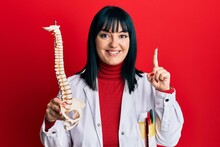 Young Hispanic Doctor Woman Holding Anatomical Model Of Spinal Column Smiling With An Idea Or Question Pointing Finger With Happy Face, Number One