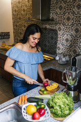 Wall Mural - Latin Woman making green smoothie or Detox juice in kitchen at Home in healthy eating concept in Mexico