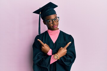 Poster - Young african american girl wearing graduation cap and ceremony robe pointing to both sides with fingers, different direction disagree