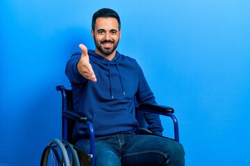 Sticker - Handsome hispanic man with beard sitting on wheelchair smiling friendly offering handshake as greeting and welcoming. successful business.