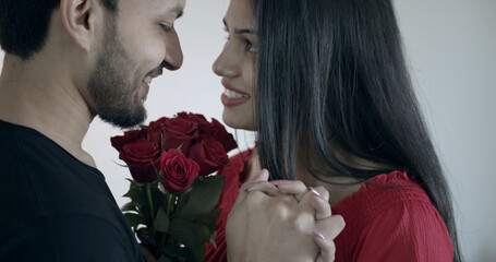 Wall Mural - Indian couple in a close position holding beautiful red flowers and spending romantic time at home