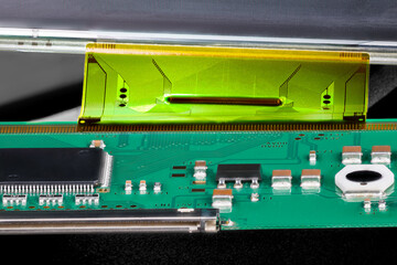 Printed circuit board connected by flexible flat cable to a LCD panel. Closeup of electronic components as micro chip, inductor or capacitor on green PCB and plastic FPC interface for digital display.