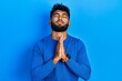 © Krakenimages.com - Arab man with beard wearing casual blue sweater begging and praying with hands together with hope expression on face very emotional and worried. begging.
