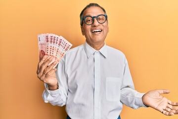 Sticker - Middle age indian man holding 100 new taiwan dollars banknotes celebrating achievement with happy smile and winner expression with raised hand